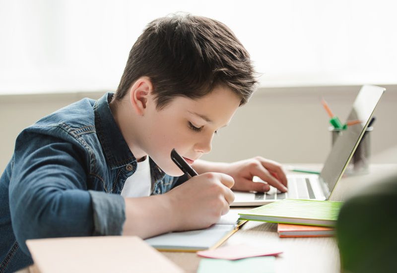Child Doing Homework with Laptop and Notepad